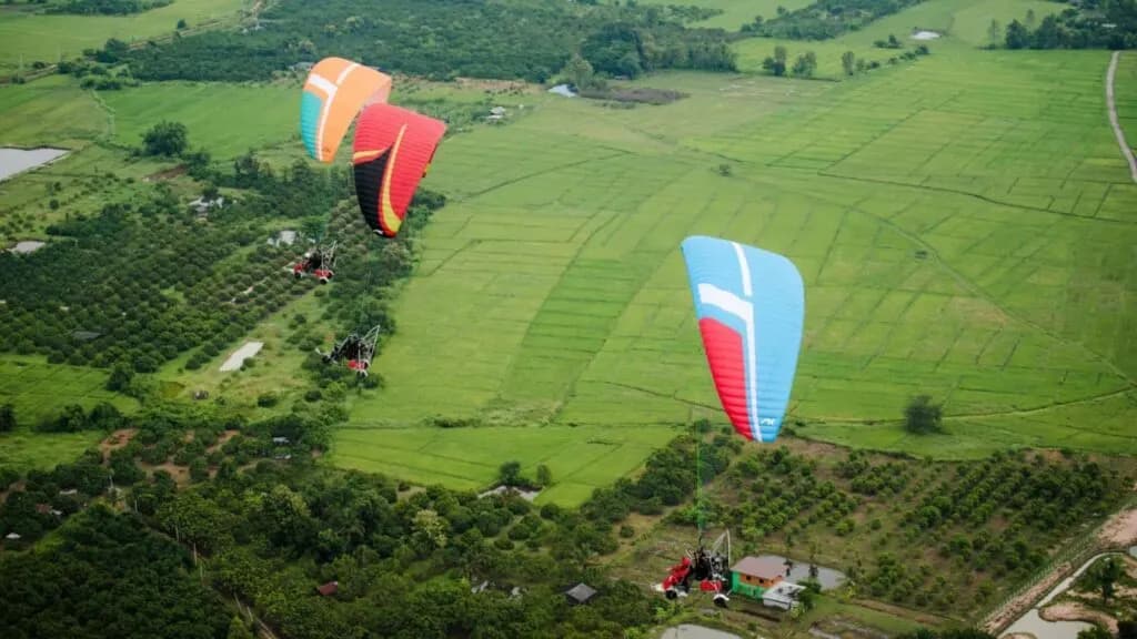 Three paramotors flying over scenic farmland, a highlight of Chiang Mai excursions