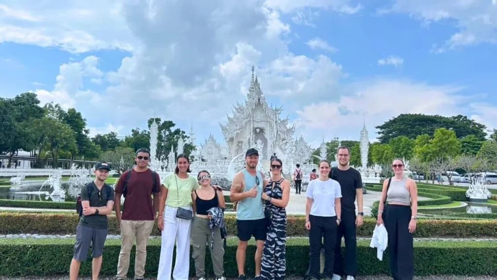 Group of tourists standing in front of the iconic White Temple (Wat Rong Khun) in Chiang Rai, Thailand, enjoying a guided tour