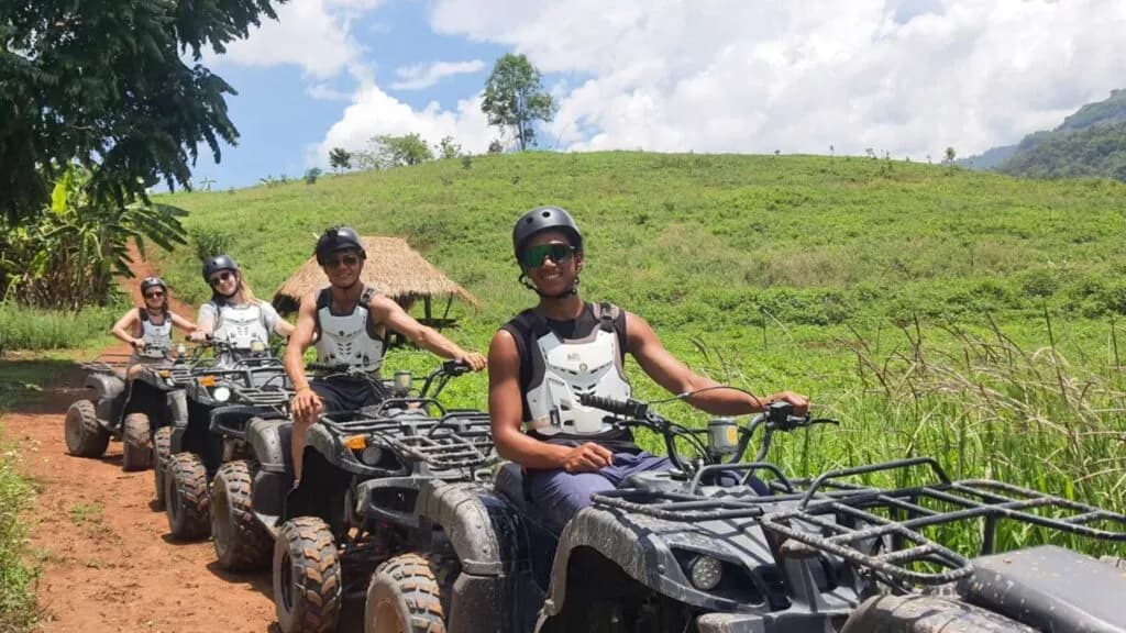 Group of travelers posing on their own ATVs with a picturesque green hill in the background, showcasing the fun of Chiang Mai tours and excursions