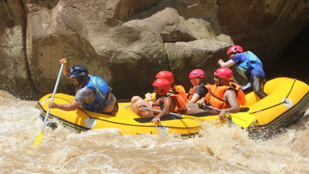 Travelers navigating rapids near a large rock on a Chiang Mai tour