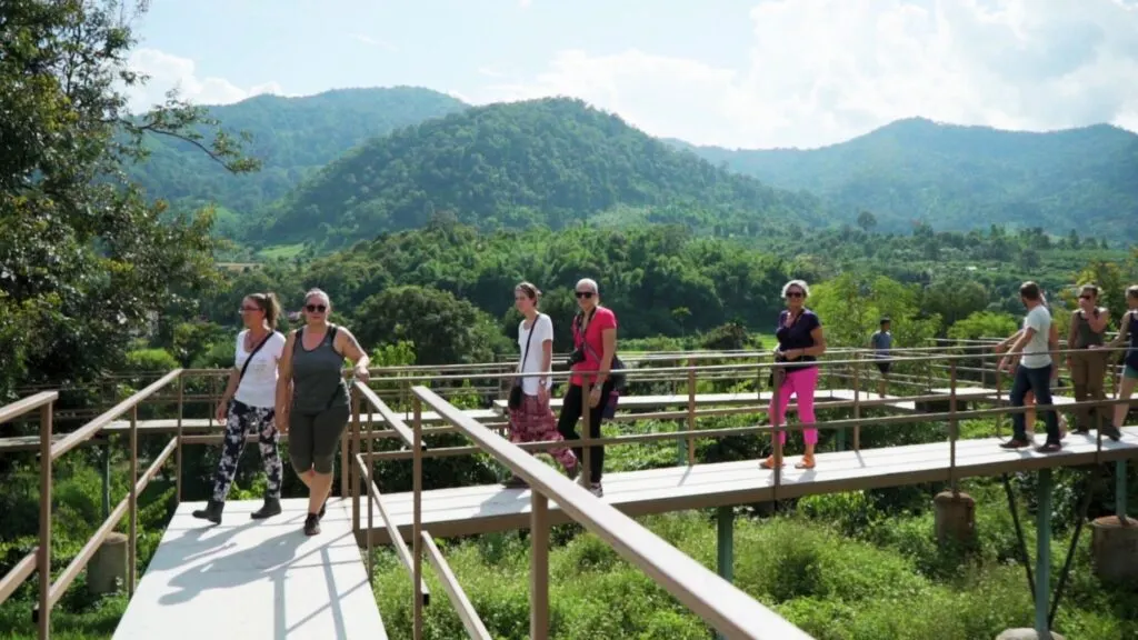 Tourists walking on an elevated walkway at the nature park, with scenic mountain views and greenery in the background, part of the Elephant Nature Park Tour in Chiang Mai