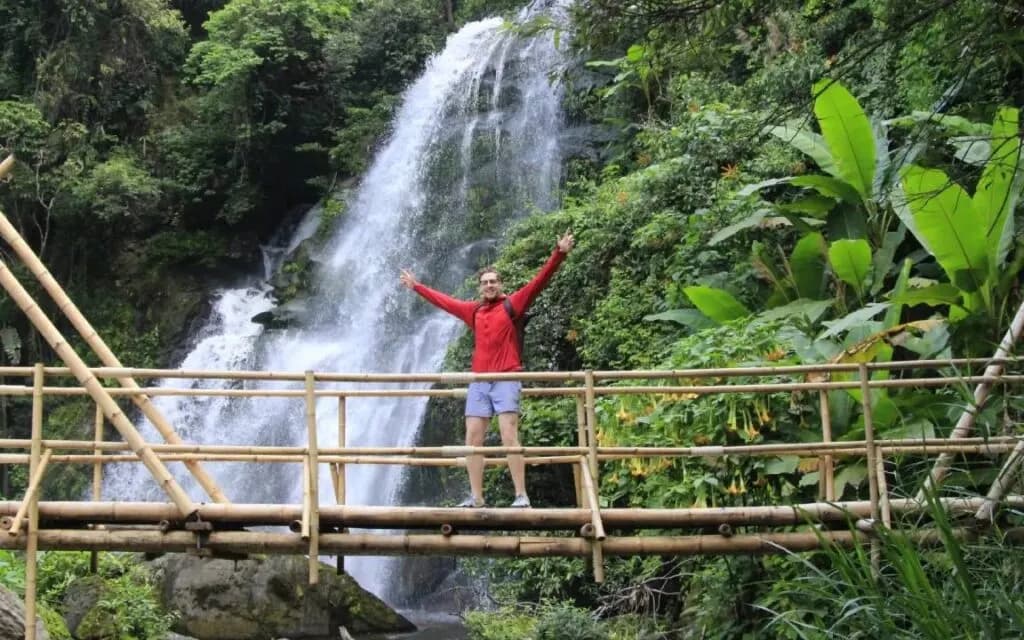 Visitor posing for a picture on a Chiang Mai trail with a big waterfall in the background, part of the Chiang Mai tour experience