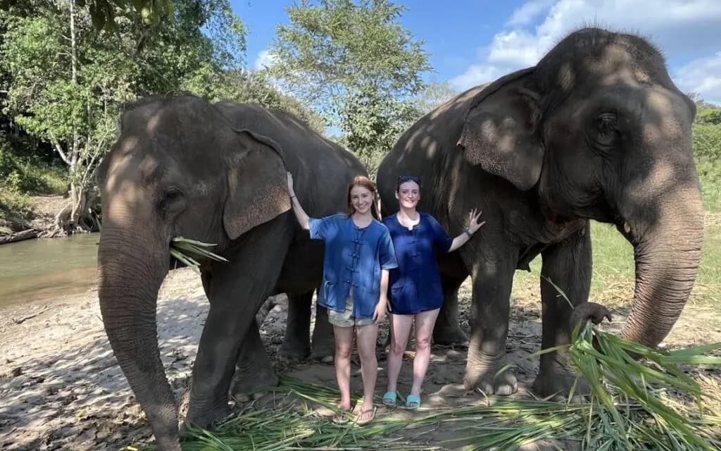Two happy tourists smiling while standing next to elephants at Living Green Elephant Sanctuary