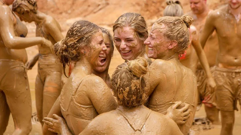 A group of tourists having fun bathing elephants in the mud pond at Maerim Elephant Sanctuary during a Chiang Mai ethical elephant experience tour.