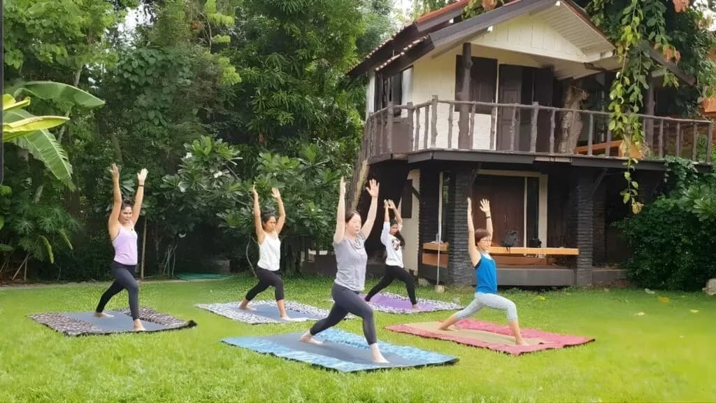 Small group yoga class on the lawn surrounded by greenery during a Chiang Mai yoga and meditation excursion.