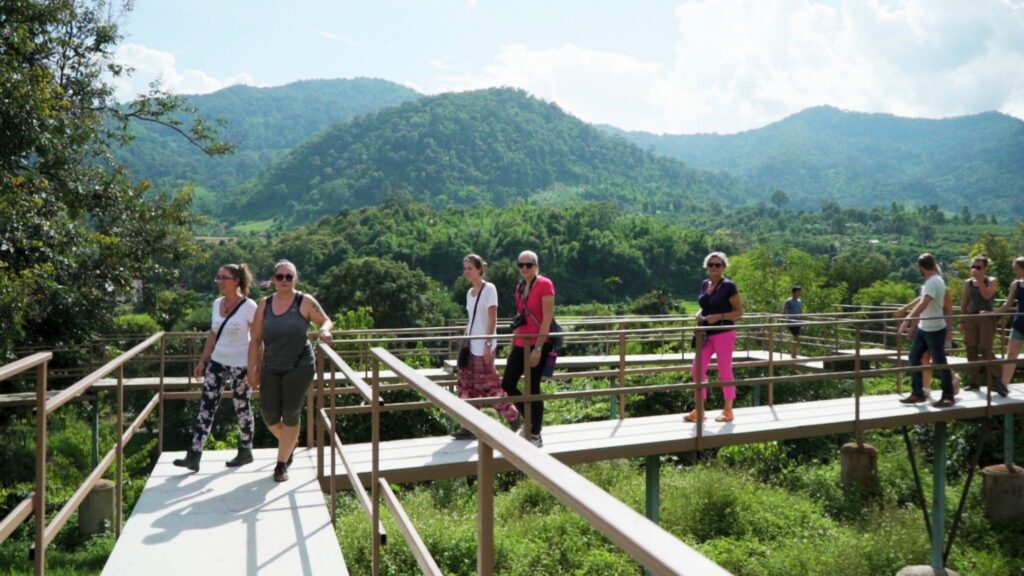 Tourists walking on an elevated walkway at the nature park, with scenic mountain views and greenery in the background, part of the Elephant Nature Park Tour in Chiang Mai