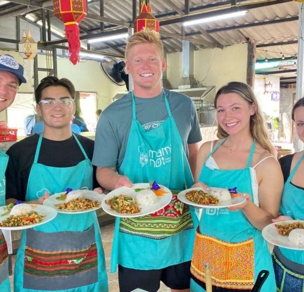 Travelers enjoying a cooking class on a Chiang Mai tour, holding plates of traditional Thai dishes they prepared.