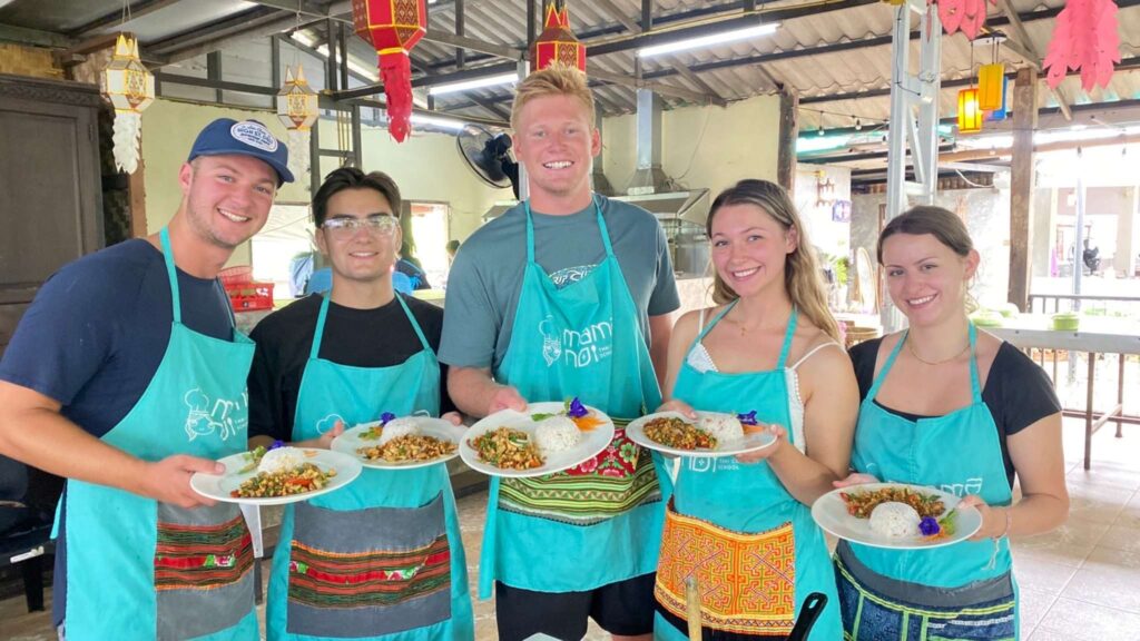 Travelers enjoying a cooking class on a Chiang Mai tour, holding plates of traditional Thai dishes they prepared.
