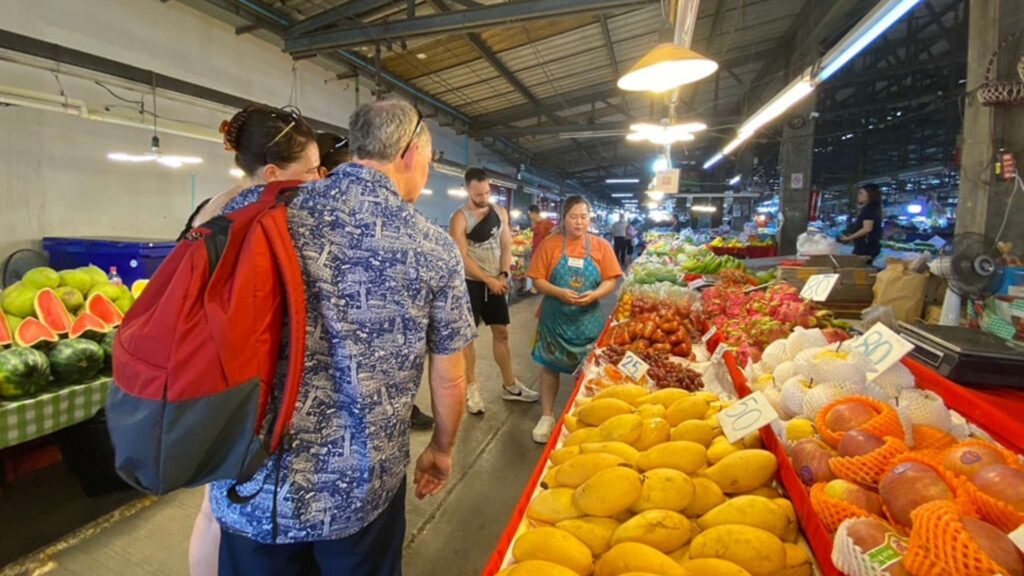 Tourists exploring a local market in Chiang Mai, learning about fresh produce as part of their Chiang Mai excursion.
