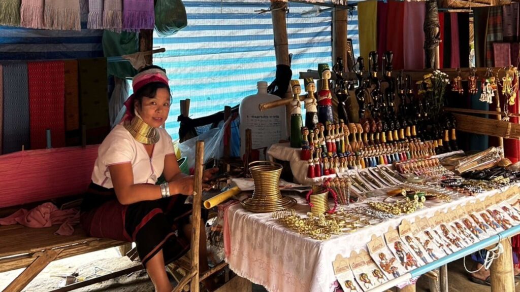 "Long-neck woman artisan displaying handmade crafts and jewelry on a cultural Chiang Mai tour, a must-see on Chiang Mai excursions