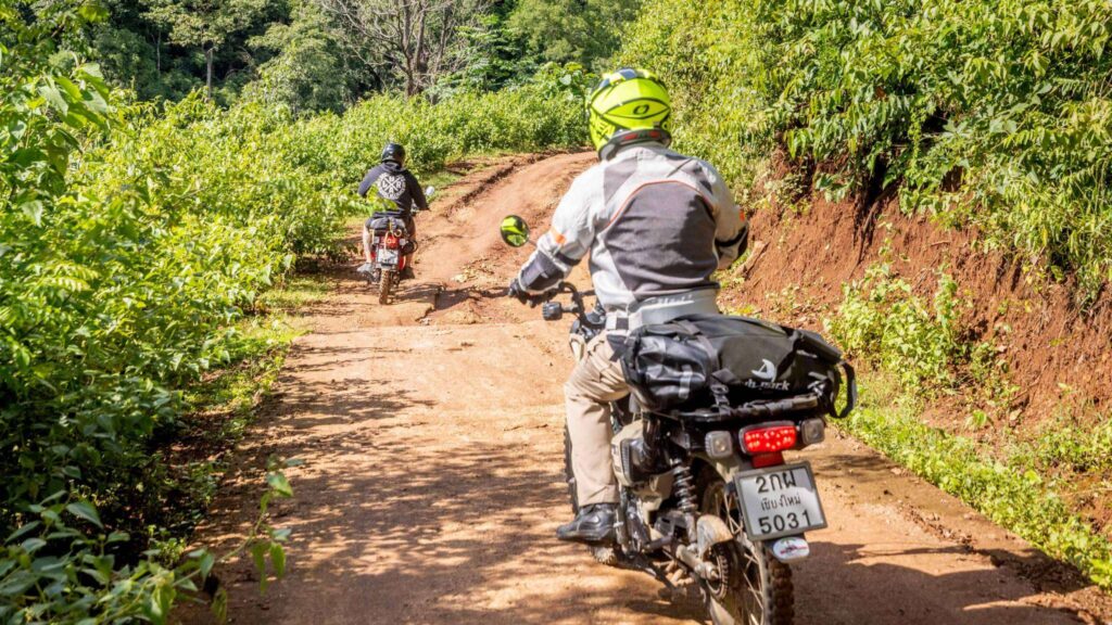 A tourist riding a scooter along a dirt road during a Chiang Mai Scooter Adventure River Cruise tour on a sunny day.
