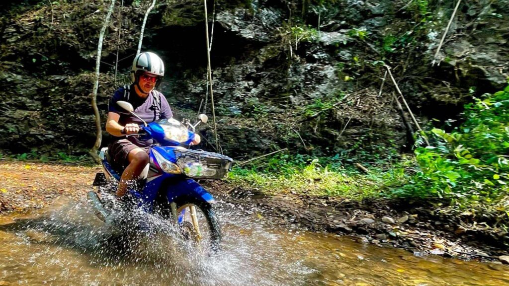 A man riding a scooter through shallow water during the Chiang Mai Scooter Adventure River Cruise tour.