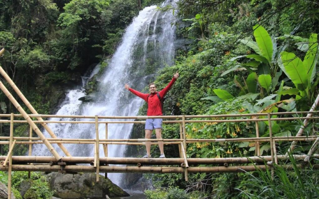 Visitor posing for a picture on a Chiang Mai trail with a big waterfall in the background, part of the Chiang Mai tour experience