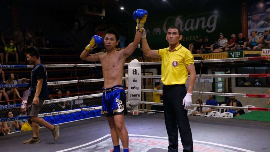 A Muay Thai champion standing tall in the ring after a thrilling win at Chiang Mai Boxing Stadium during your Chiang Mai excursion.