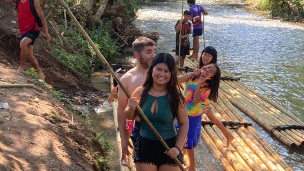 A group of travelers smiles happily while standing on bamboo during a Chiang Mai tour at an elephant sanctuary.